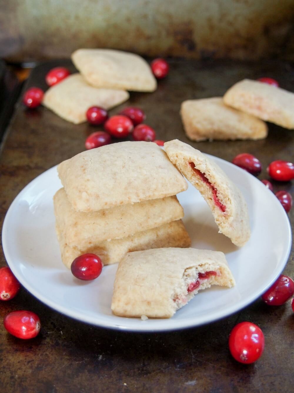 cranberry jam filled shortbread cookies on plate with two bitten into resting on side and in front of stack