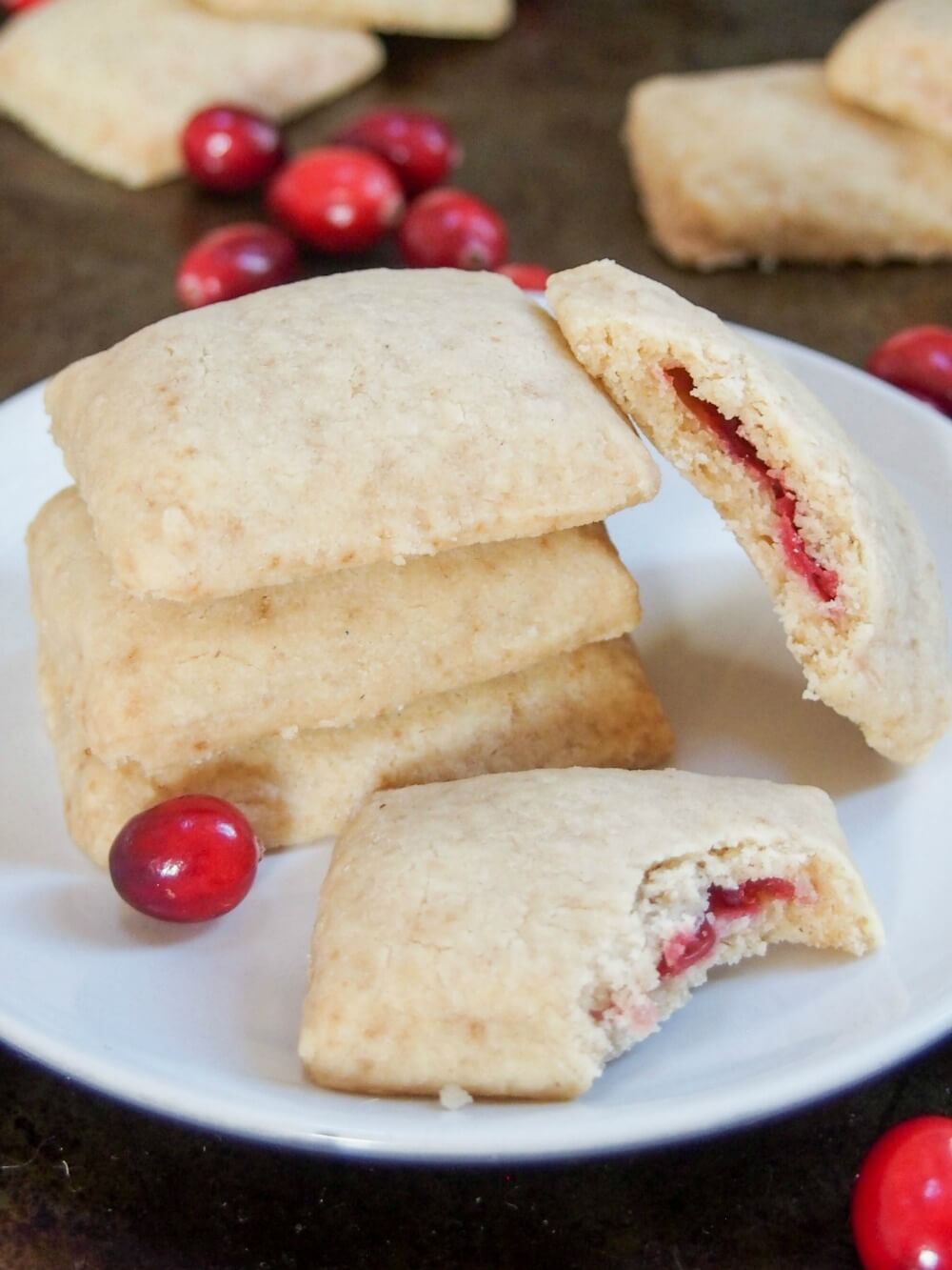cranberry jam filled shortbread cookies in stack on plate with bitten cookies showing filling