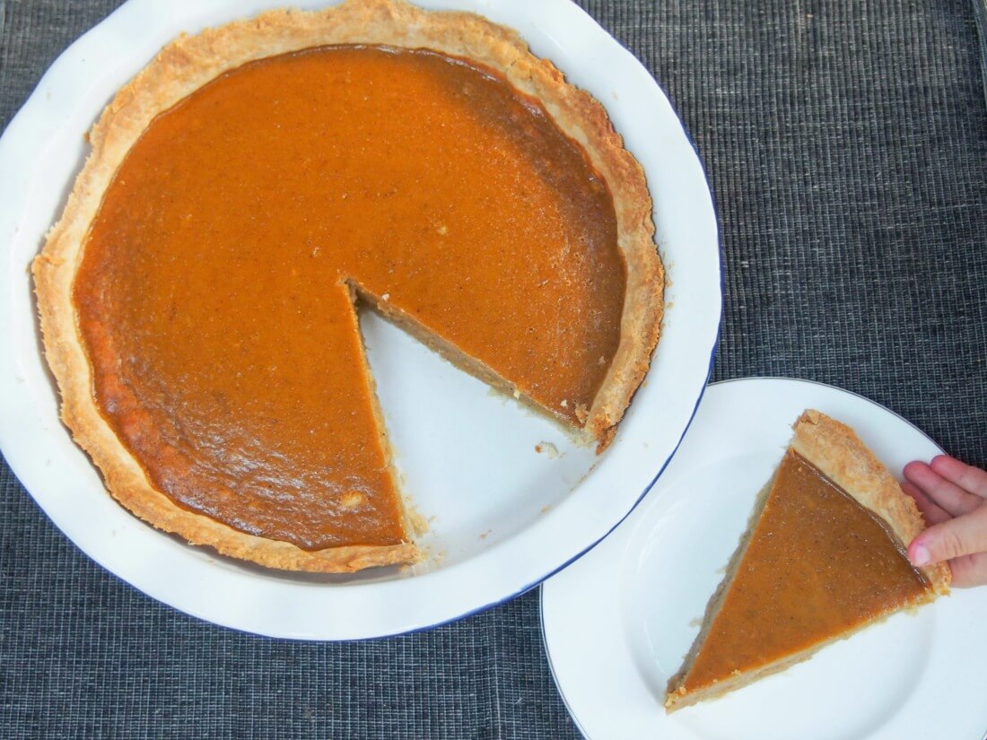 pumpkin pie with slice cut out on plate to side and toddler hand grabbing slice