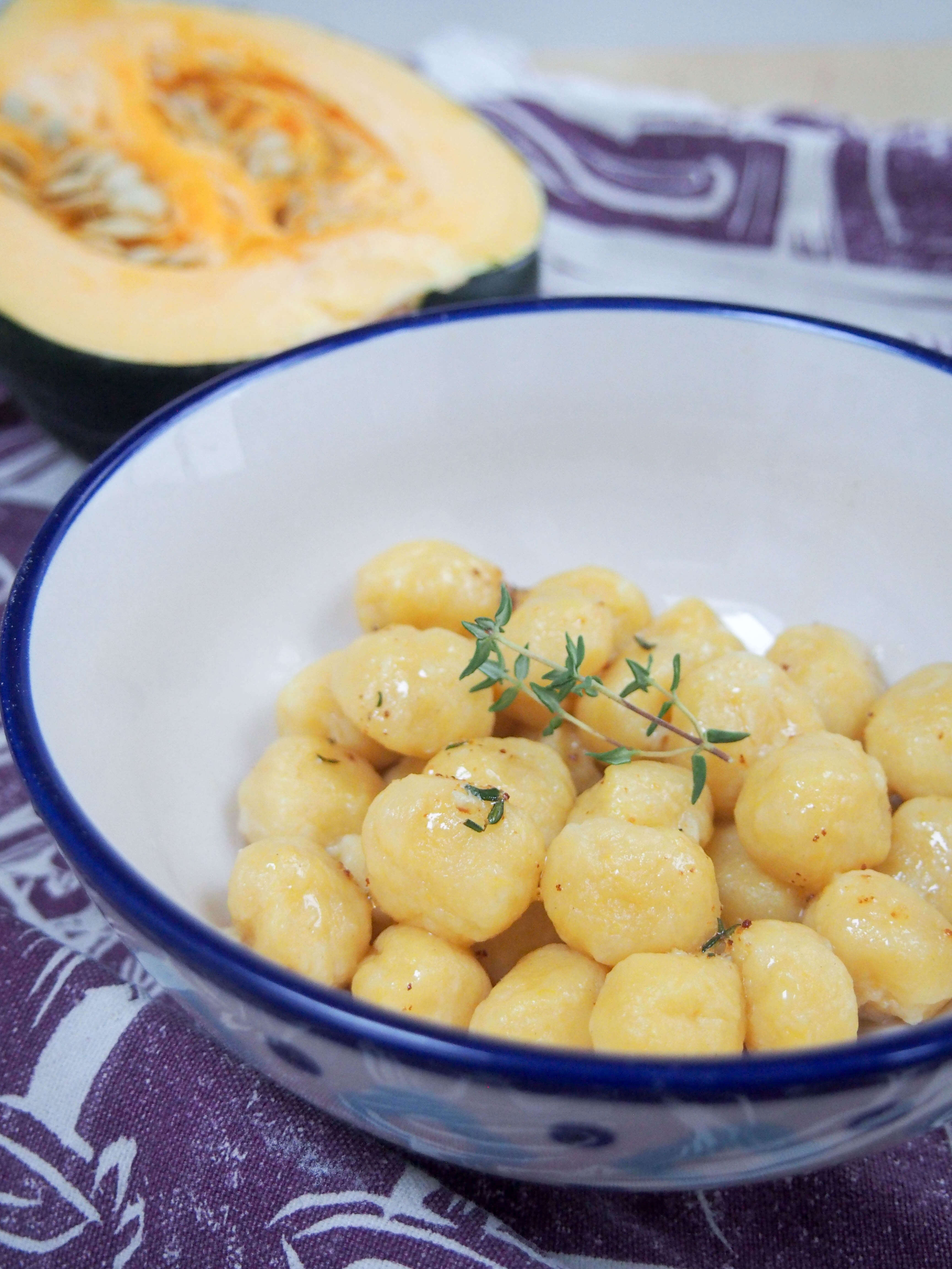 Side view of bowl of gnocchi topped with sprig of thyme