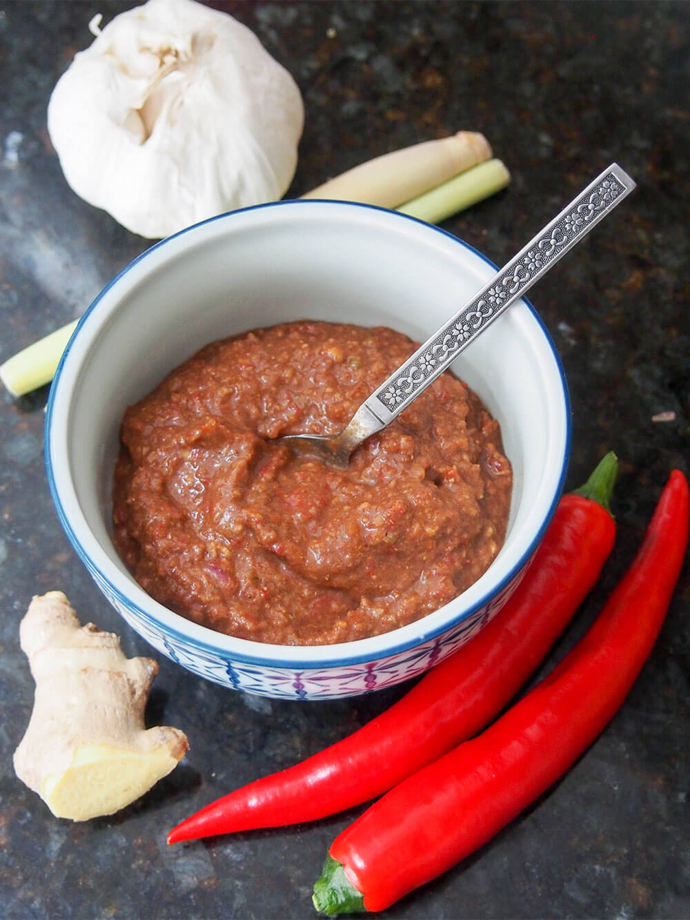 dish of homemade Thai red curry paste with chilis, ginger, garlic and lemongrass around dish