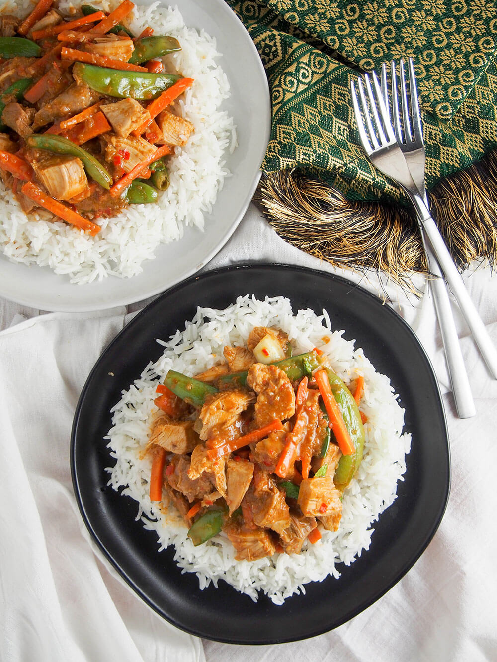 two plates of Thai red curry served over rice with forks to side, viewed from overhead