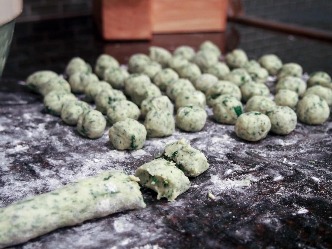 making potato spinach gnocchi - log of dough with some pieces chopped off and formed gnocchi behind