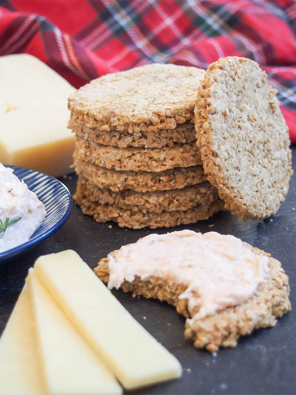 stack of oatcakes with pate on one of the crackers and pieces of cheese in front