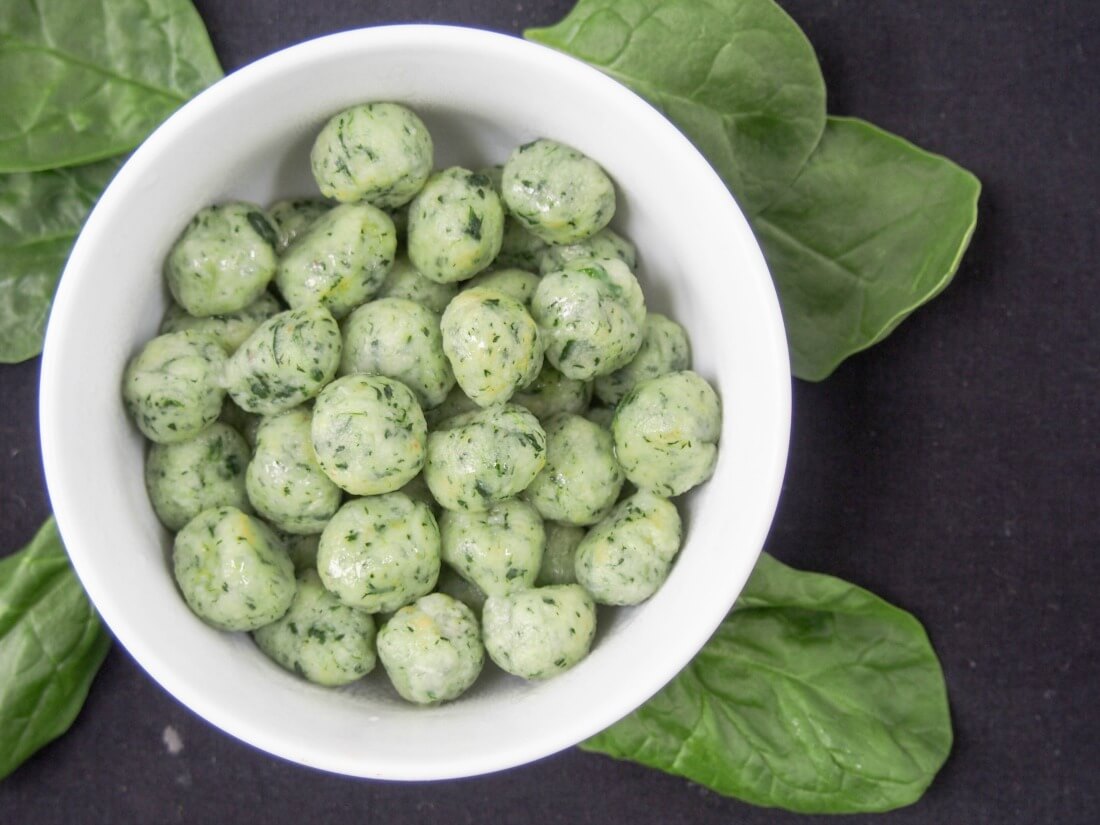 bowl of potato spinach gnocchi viewed from overhead with spinach leaves around bowl