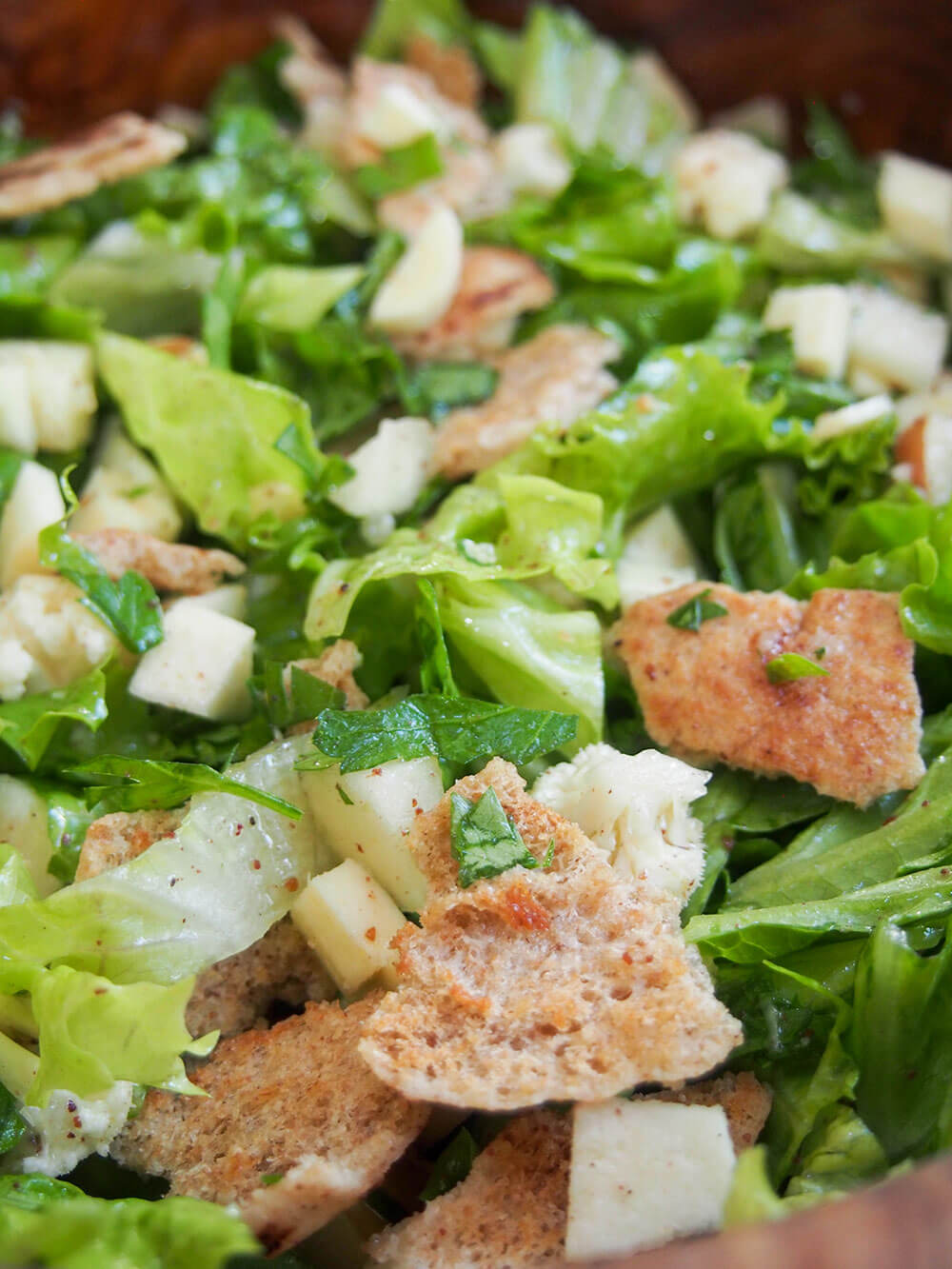 close up showing pieces of bread and fleks of sumac in dressing on salad