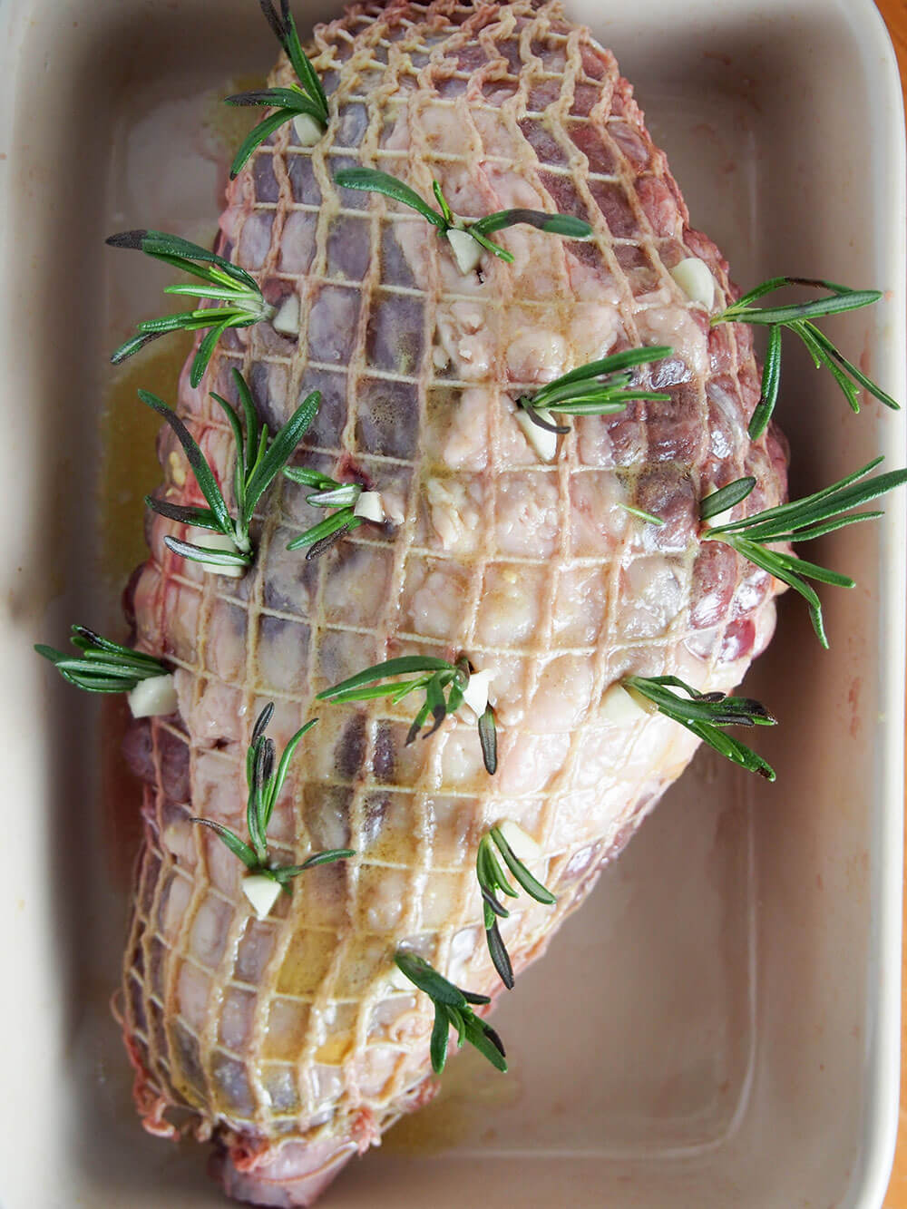 preparing roast lamb with pieces of garlic and rosemary studded in roast