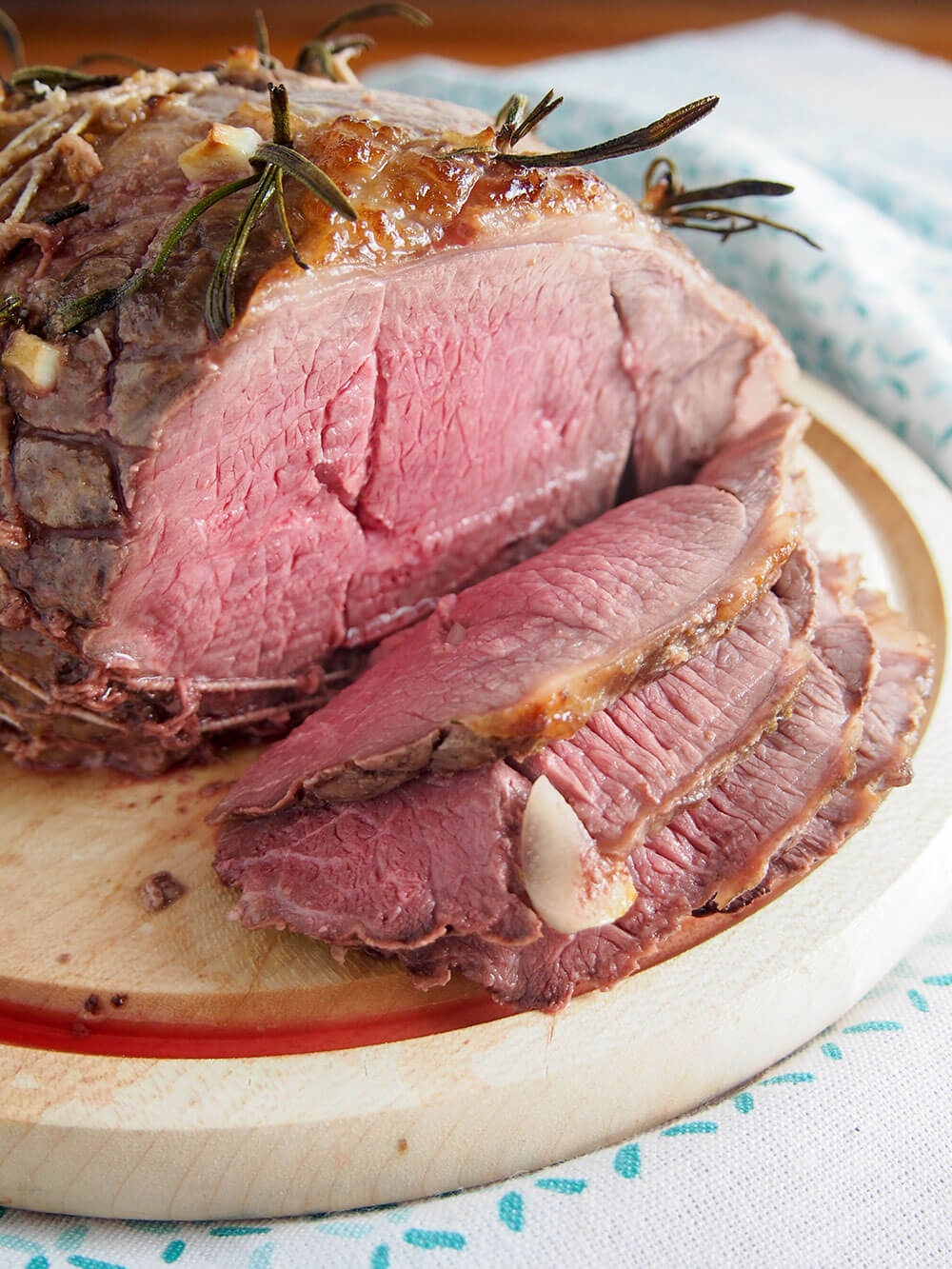 close up of slices of roast lamb with pieces of rosemary and garlic studded on top of main roast