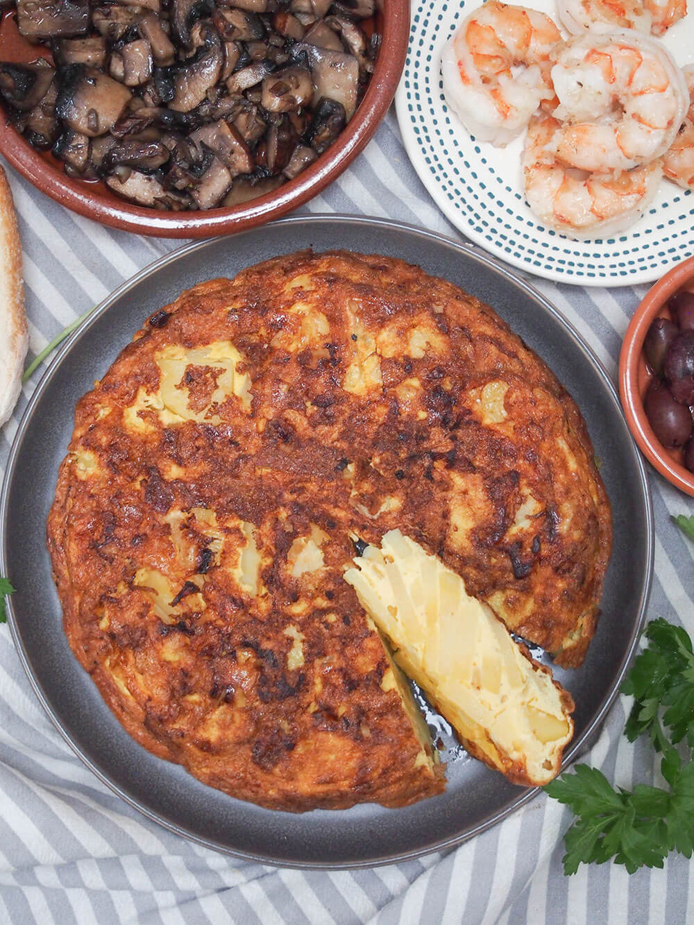 This simple yet tasty Spanish tortilla (tortilla Española) can be made with traditional potato or swap it for rutabaga for a lower carb version. It's great as part of a tapas meal, or take it on a picnic or to a party. Versatile, comforting and so good. Spanish tortilla, tortilla Española, viewed from above with shrimp and mushrooms in dishes above