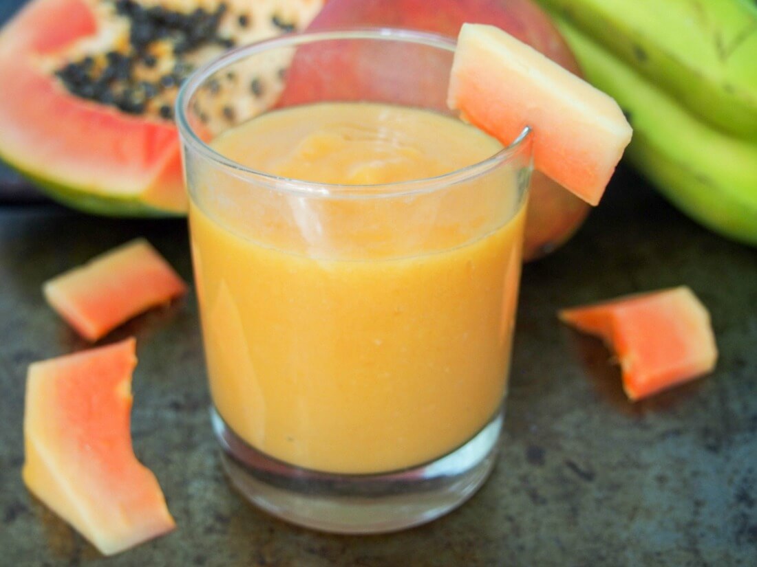 This tropical fruit smoothie is made with mango and papaya for a refreshing, tasty and vitamin-C packed drink. Made just with fruit and fruit juice, with an optional boost from flax seeds, it's also naturally dairy free. Delicious and good for you all in one. glass of tropical fruit smoothie with papaya pieces around and whole fruit behind