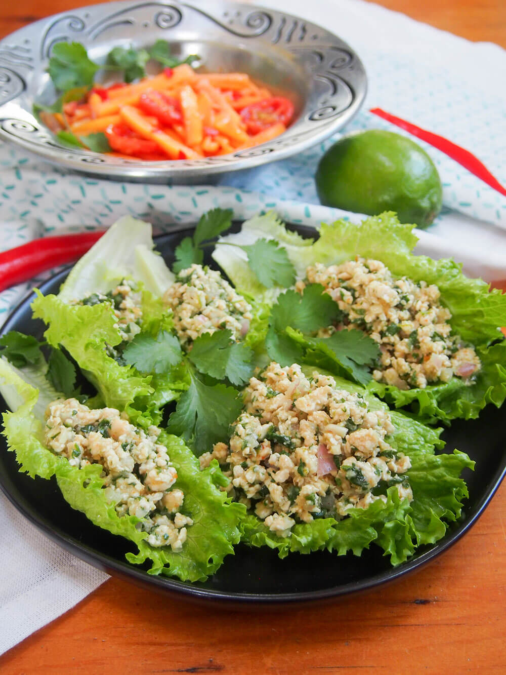 Larp (larb gai, Thai/Laos chicken salad) served on lettuce leaves with papaya salad behind
