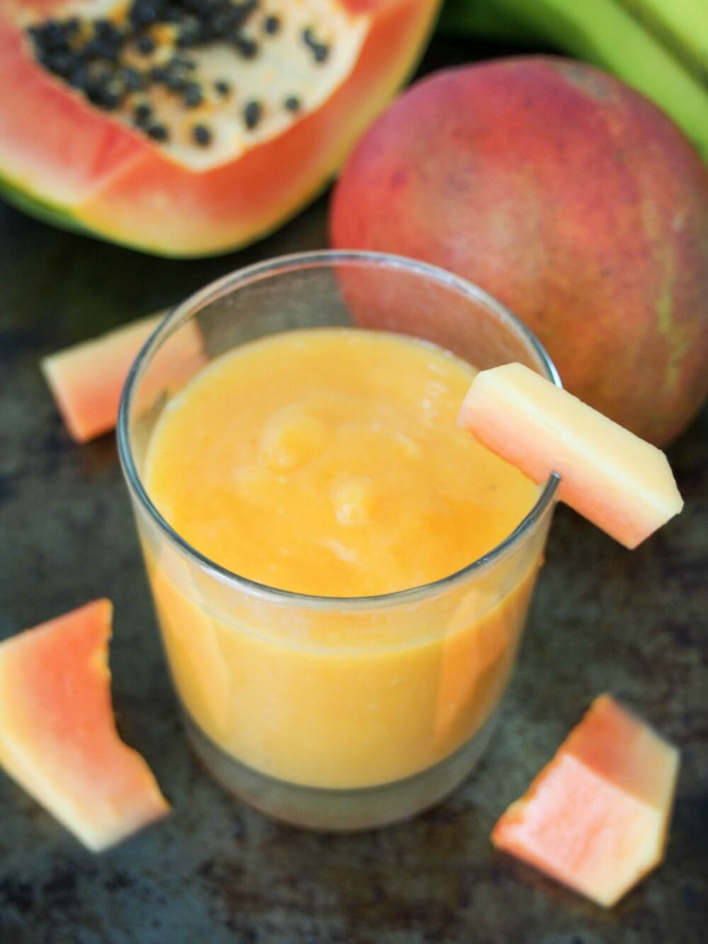 This tropical fruit smoothie is made with mango and papaya for a refreshing, tasty and vitamin-C packed drink. Made just with fruit and fruit juice, with an optional boost from flax seeds, it's also naturally dairy free. Delicious and good for you all in one. glass of tropical fruit smoothie with papaya and mango behind