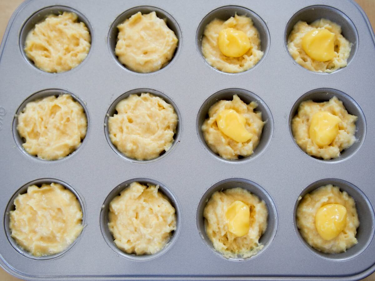 making mini lemon almond muffins - half completely filled, other half with spoonful of lemon curd sitting on top of part of batter ready to be covered
