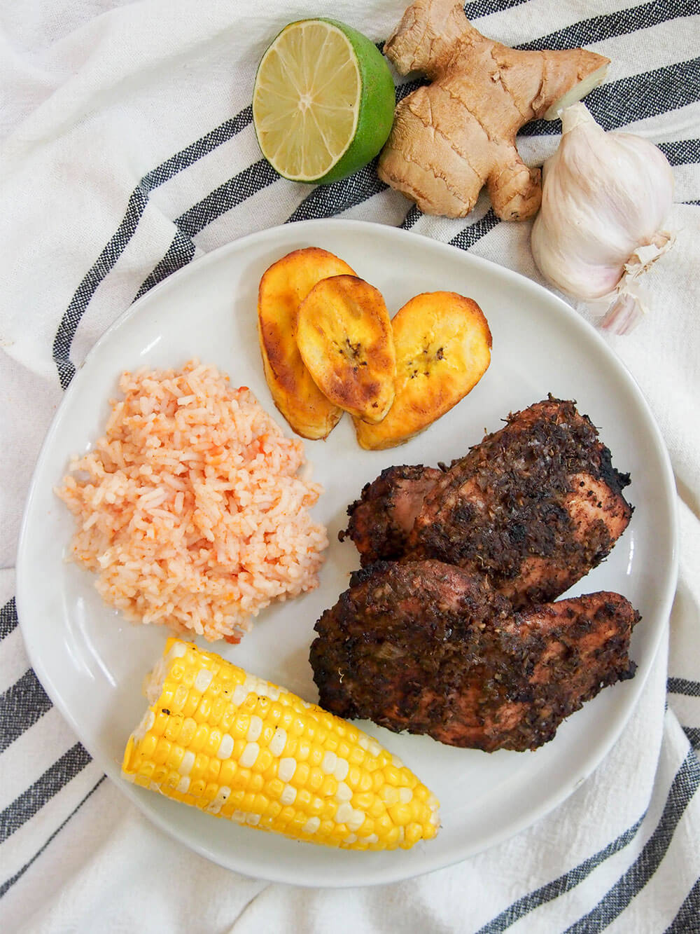Plate of Jamaican jerk chicken, rice, corn and plantain viewed from above