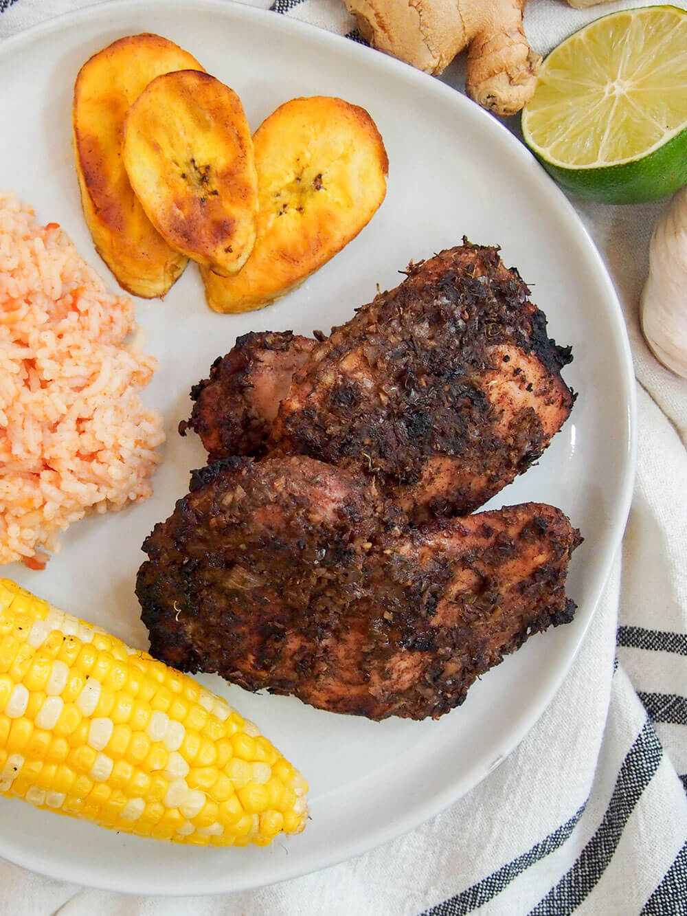 Jamaican jerk chicken on plate with partial view of sides