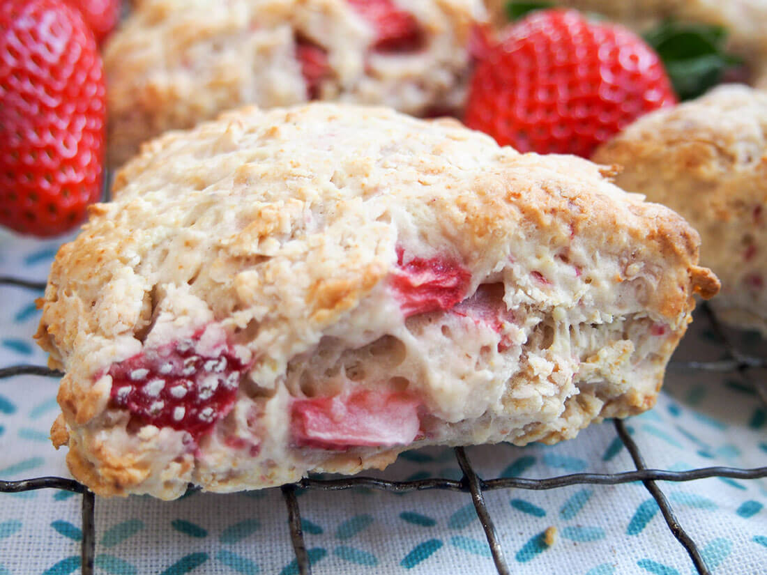 These strawberry scones are made with mascarpone and a double doze of strawberries for a wonderfully soft, fruity mouthful in every bite. Easy to make, they're a wonderful snack. close up of strawberry scone with mascarpone showing chunks of strawberry sticking out side