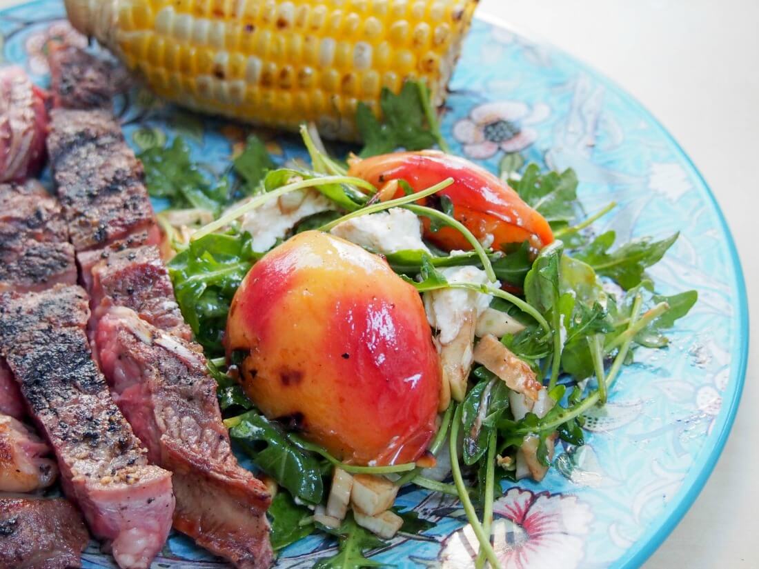 grilled nectarine salad served as side to steak with corn cob behind