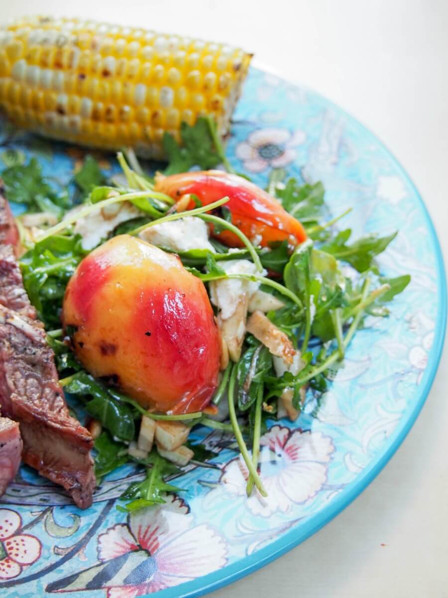 grilled nectarine salad served on plate as a side to steak with corn cob behind