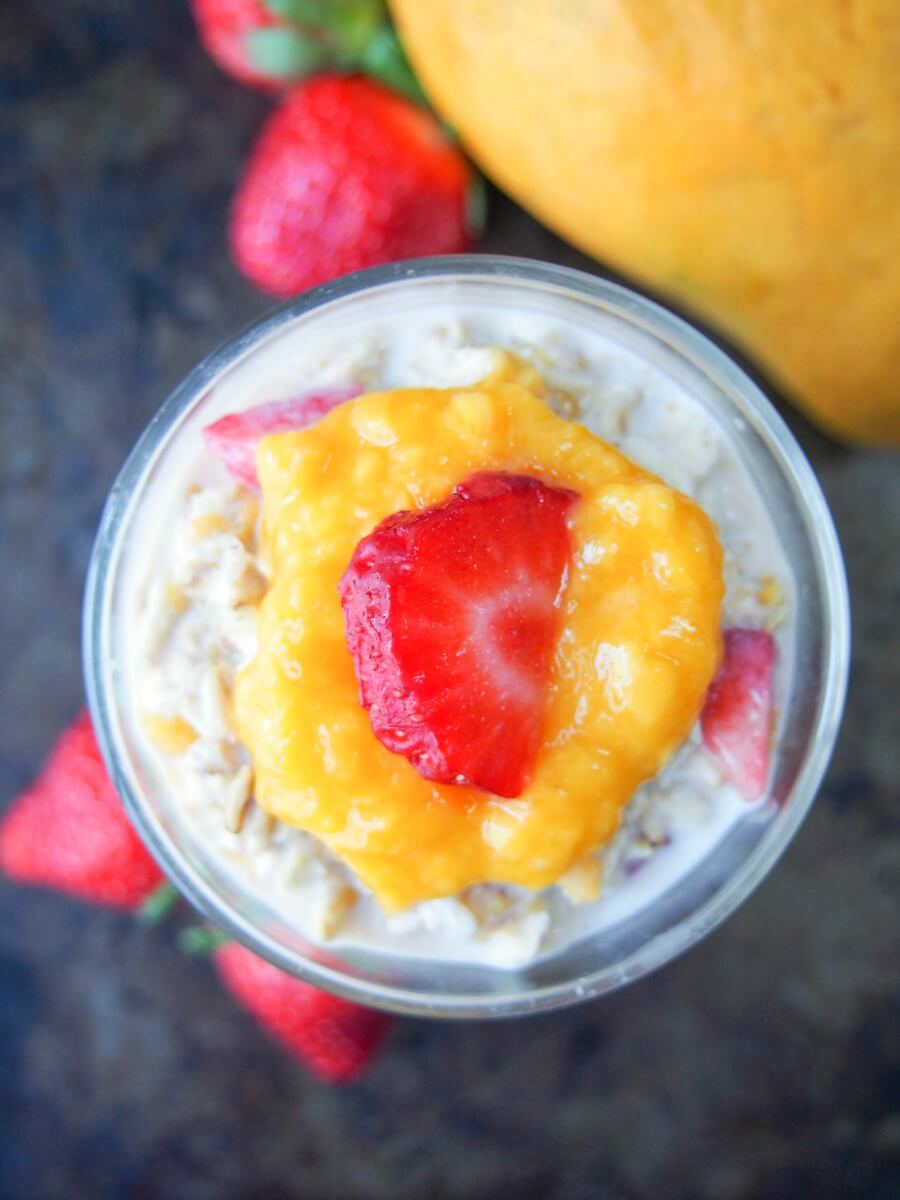 This mango and strawberry overnight oats is the perfect light breakfast for warmer weather. Deliciously smooth, creamy, fresh & fruity. And so easy to make! glass of mango and strawberry overnight oats from overhead with mango and strawberries to side