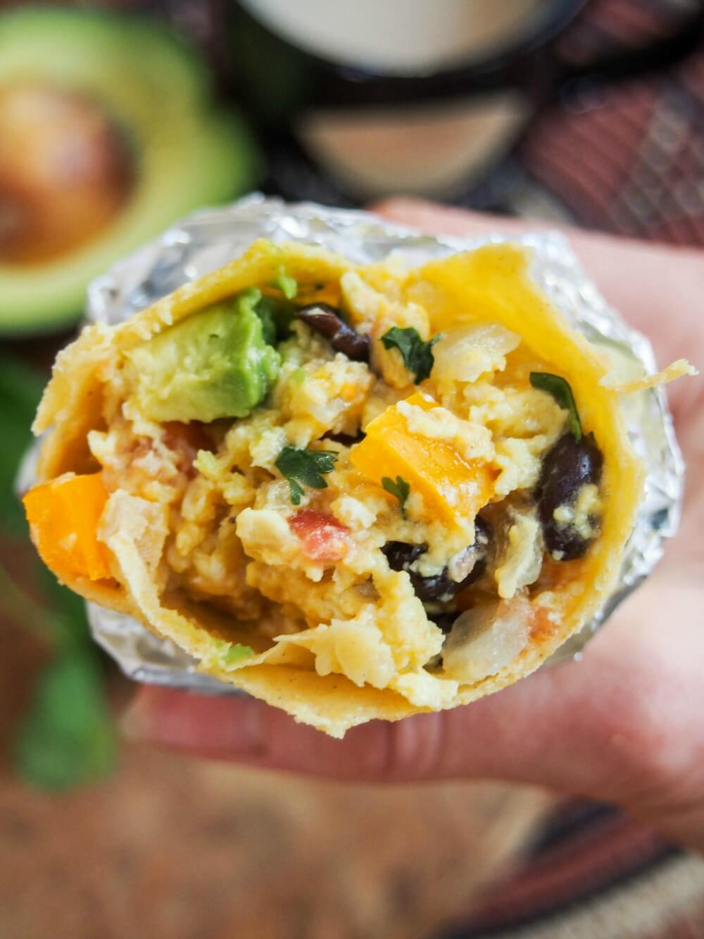 vegetarian breakfast burrito held in hand and bitten into showing filling