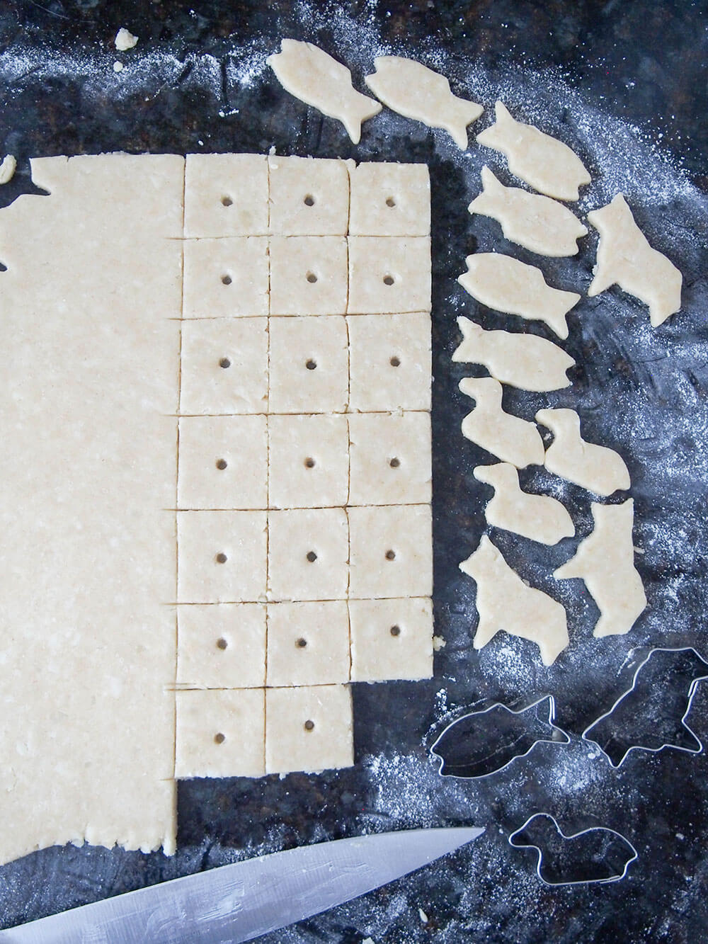 cutting homemade cheese crackers - some in squares, others with mini animal cutters