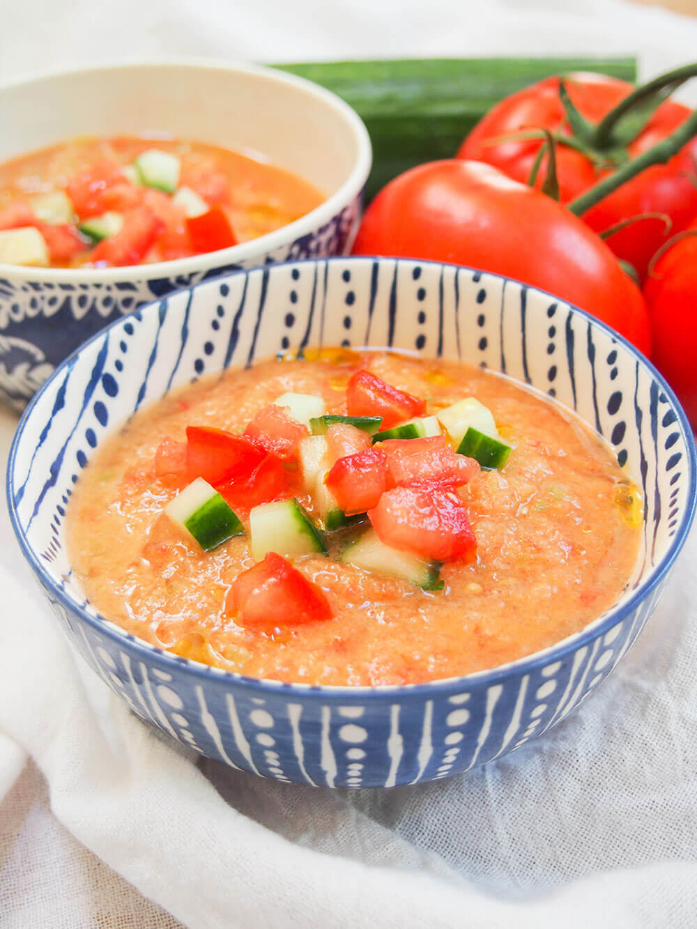 bowls of gazpacho topped with cucumber, tomato and a drizzle of olive oil from front