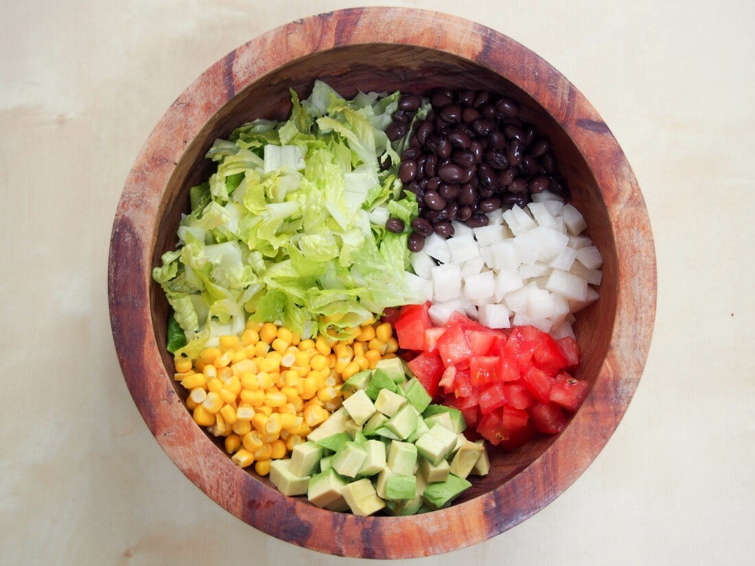 salad ingredients in piles within bowl before mixing