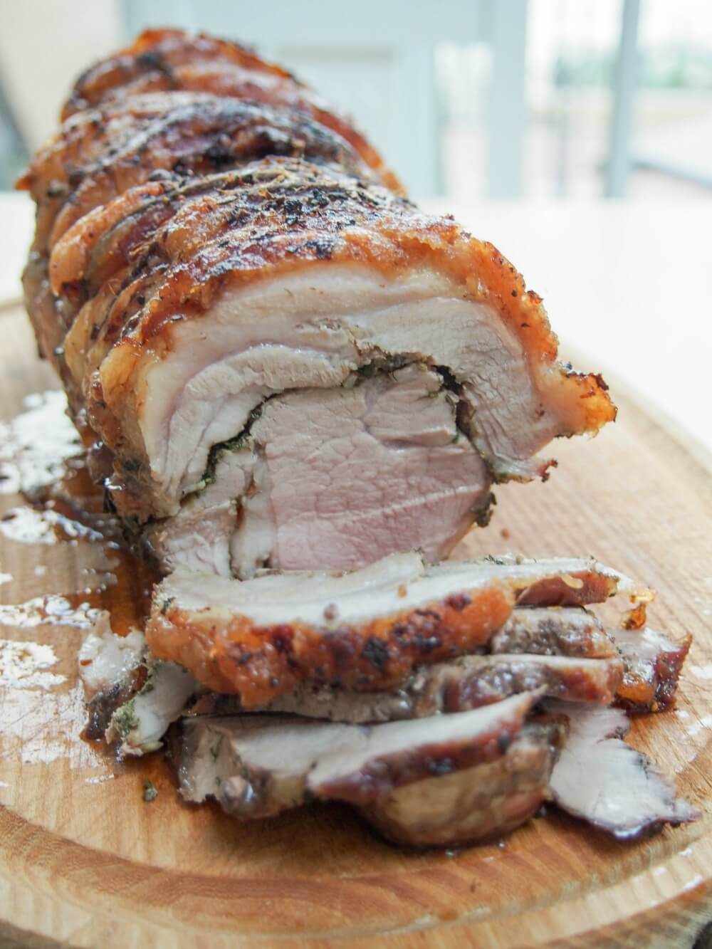 porchetta with some cut slices at front and rest of roast behind, looking at cut edge as it sits on cutting board