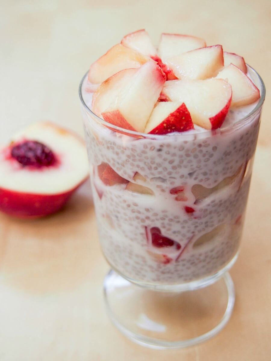 coconut chia pudding with white peach pieces on top and in layers in middle, viewed from side