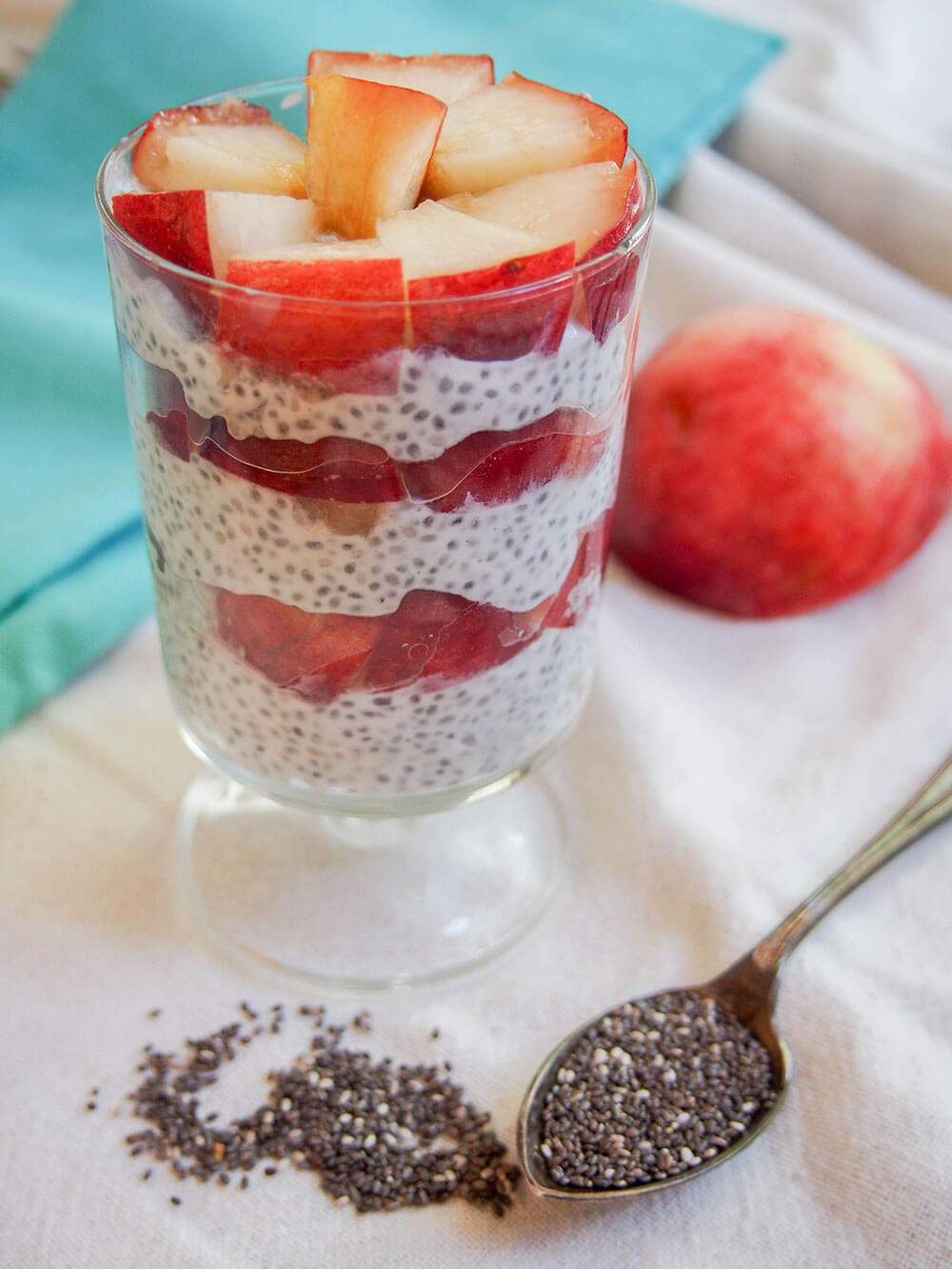coconut chia pudding with white peach layers with chia seeds on spoon below glass