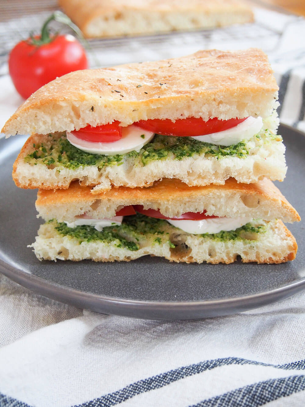focaccia sandwich filled with tomato, mozzarella and pesto with one piece stacked on top of other