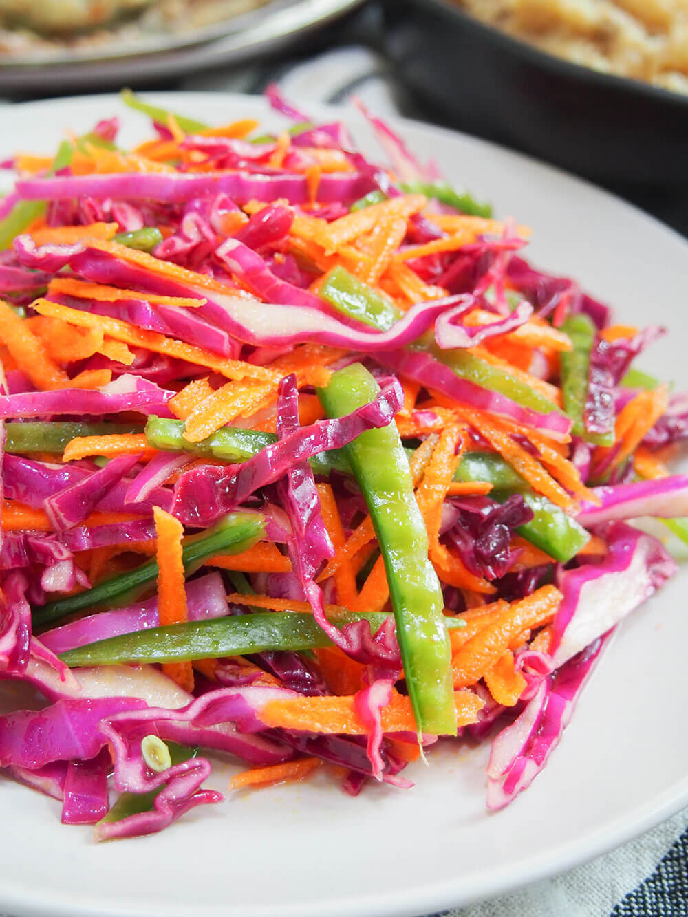 This rainbow slaw has only a few ingredients, but is both bright on your plate and in your mouth. Easy, crunchy and flavorful, it's versatile and great for potlucks and more. close up view of rainbow slaw on plate