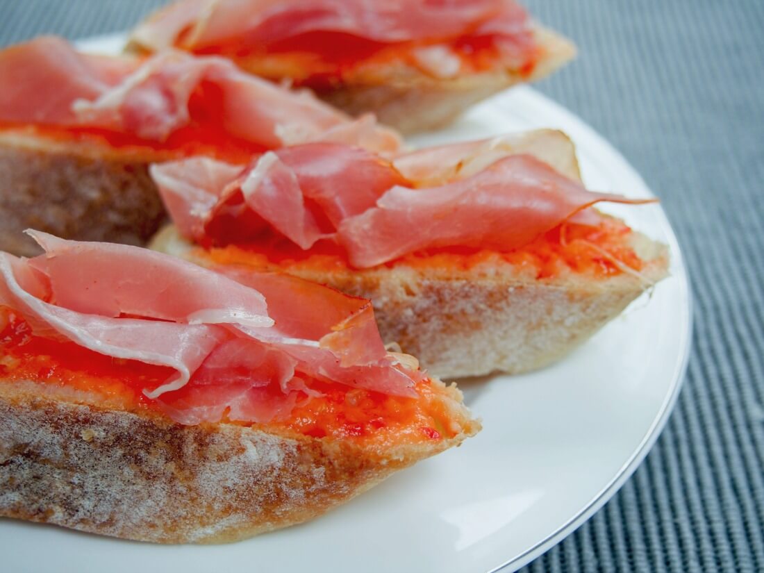 pieces of pan con tomate (tomato bread) topped with serrano ham