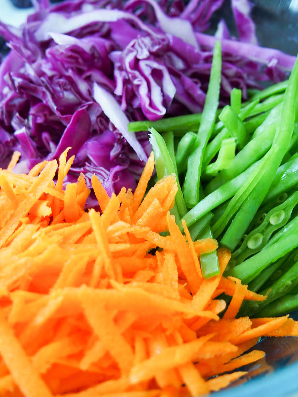 cut up vegetables for rainbow slaw in bowl shredded cabbage, grated carrot and sliced snow peas in stacks