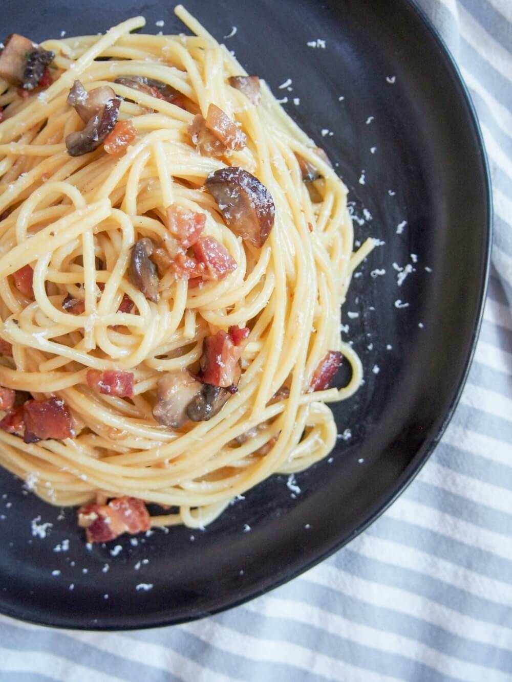 Stack of spaghetti alla carbonara with mushrooms on plate from above