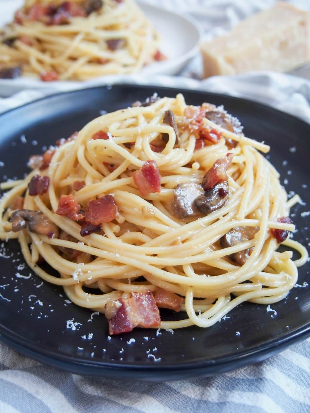 Spaghetti alla carbonara with mushrooms on black plate with another plate behind