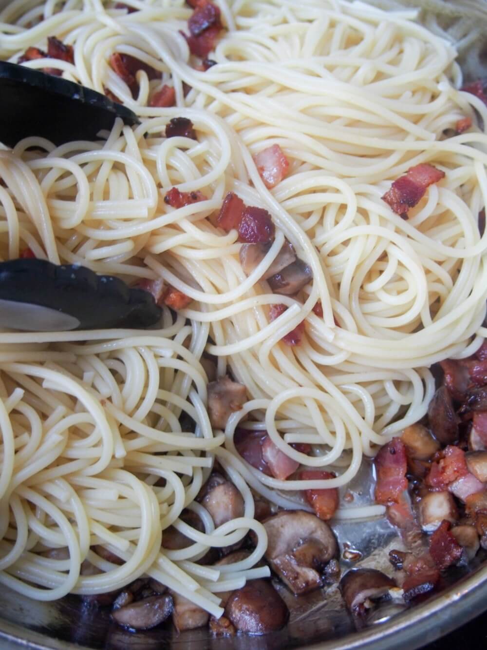 adding pasta to pan with bacon and mushrooms