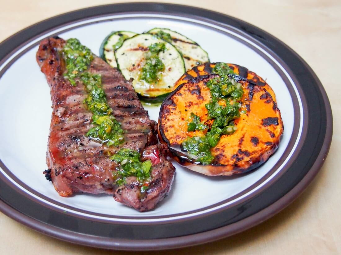 grilled butternut squash, zucchini & steak with chimichurri sauce drizzled over top, all on plate