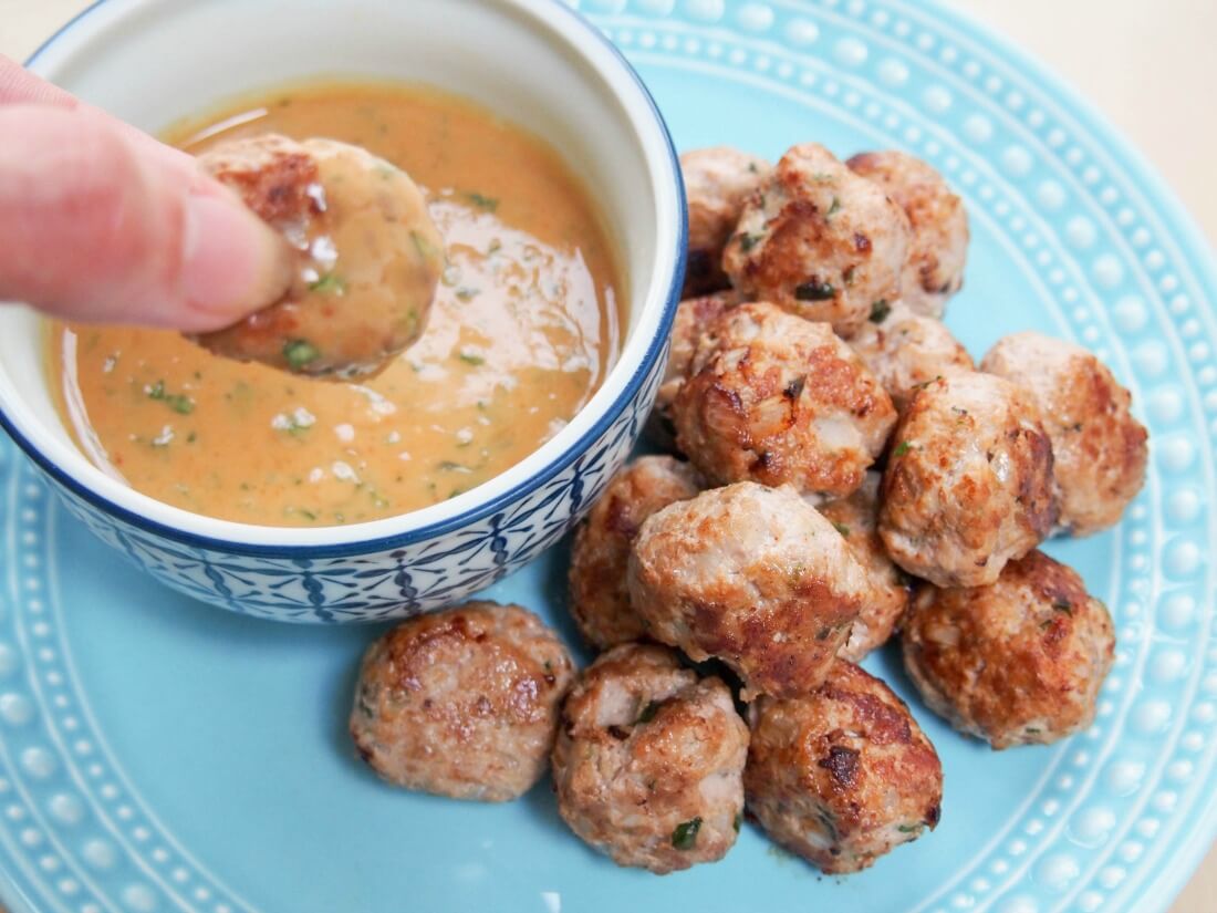 dipping a meatball into sauce with stack of meatballs on plate to side