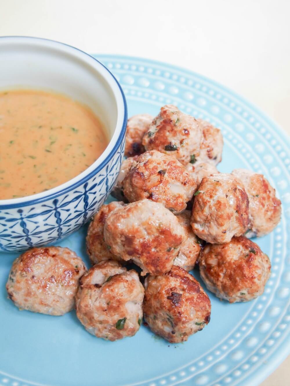 stack of Thai basil pork meatballs with peanut-basil sauce to side