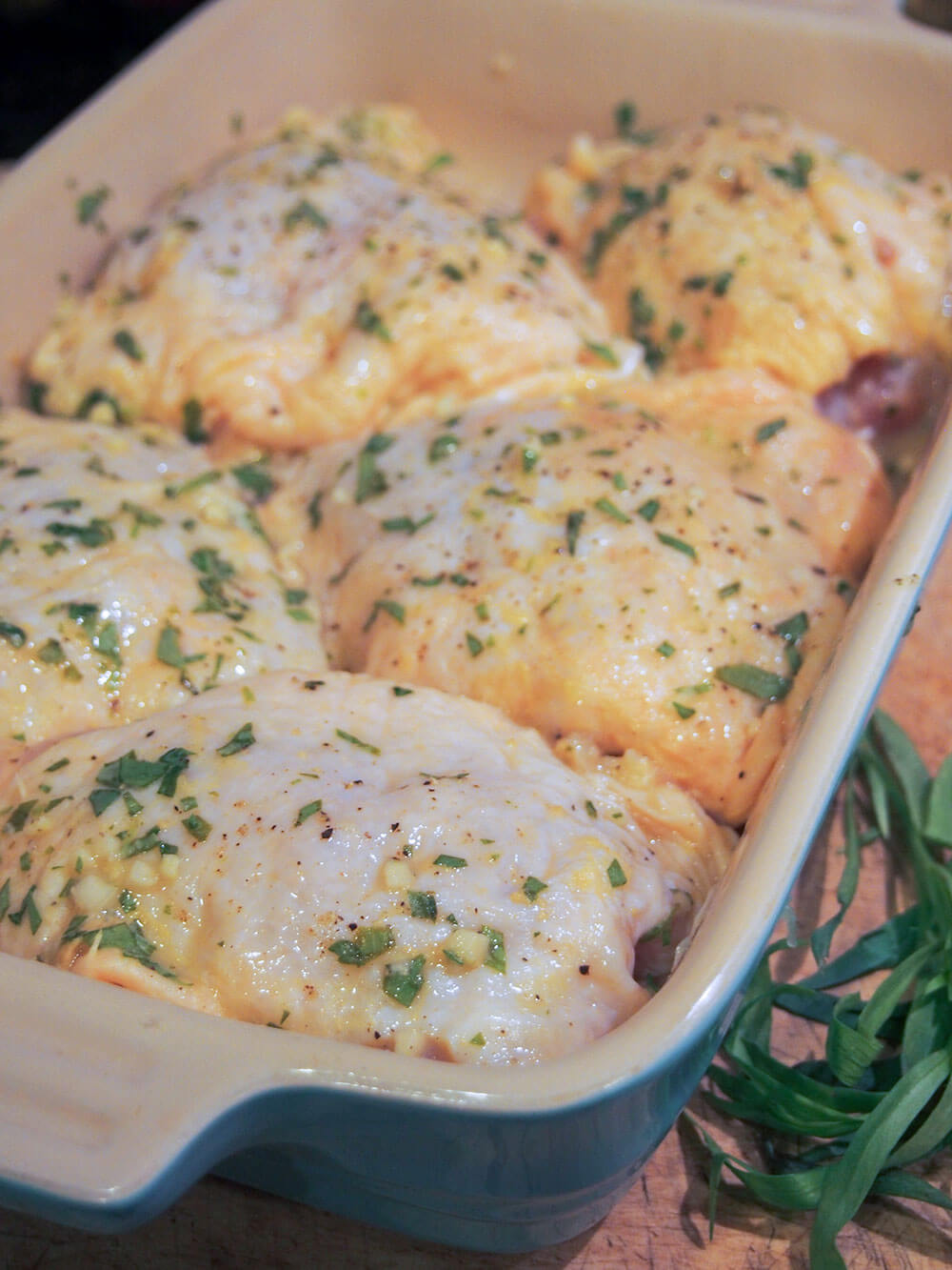 preparing tarragon chicken chicken thighs in baking dish with marinade over them, ready to bake