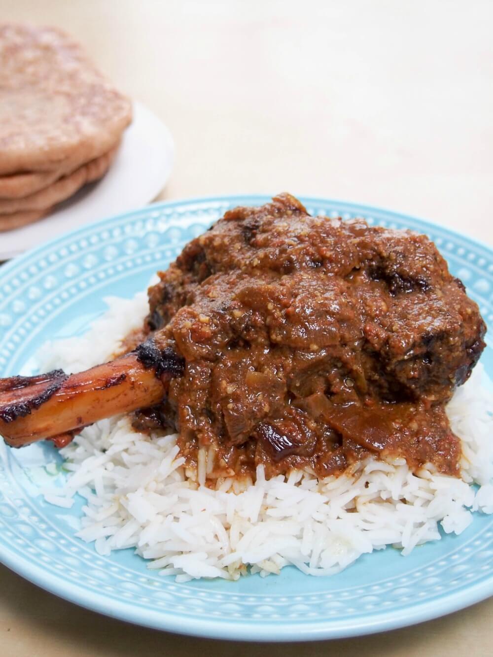 Slow cooker lamb rogan josh on plate over rice with naan behind