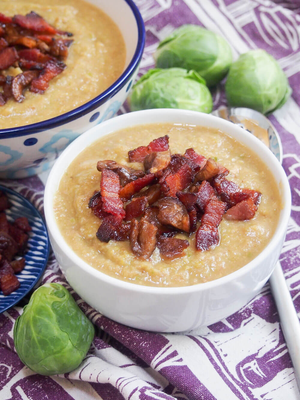 bowl of Brussel sprout soup with crispy bacon and chestnut on top and Brussel sprouts behind