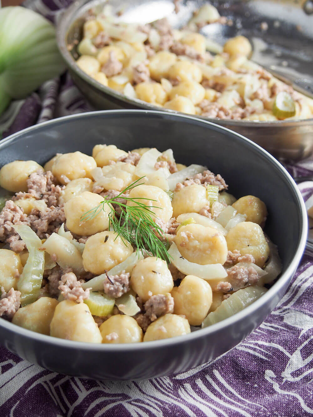 bowl of gnocchi with pork and fennel with skillet with more in behind