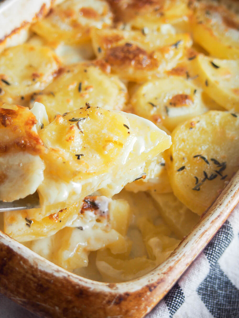 Dauphinoise potatoes are a wonderful combination of creamy potatoes with a touch of garlic and thyme. Rich, meltingly tender and so good. taking a spoonful from dish of Dauphinoise potatoes