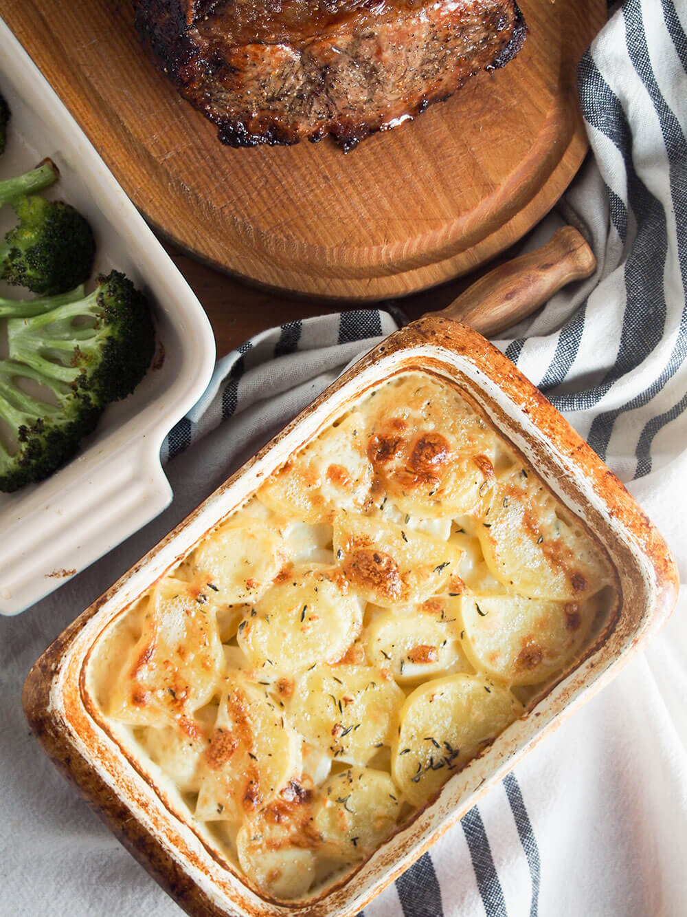 Dauphinoise potatoes are a wonderful combination of creamy potatoes with a touch of garlic and thyme. Rich, meltingly tender and so good. Dauphinoise potatoes served alongside roast beef and broccoli viewed from overhead