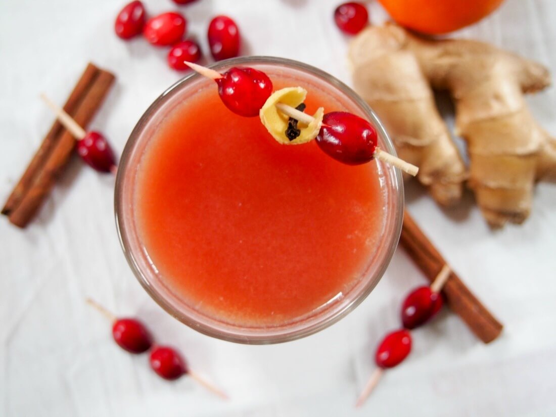 Warm spiced cranberry cocktail  with cranberries on cocktail stick as garnish from overhead with spices to side of glass