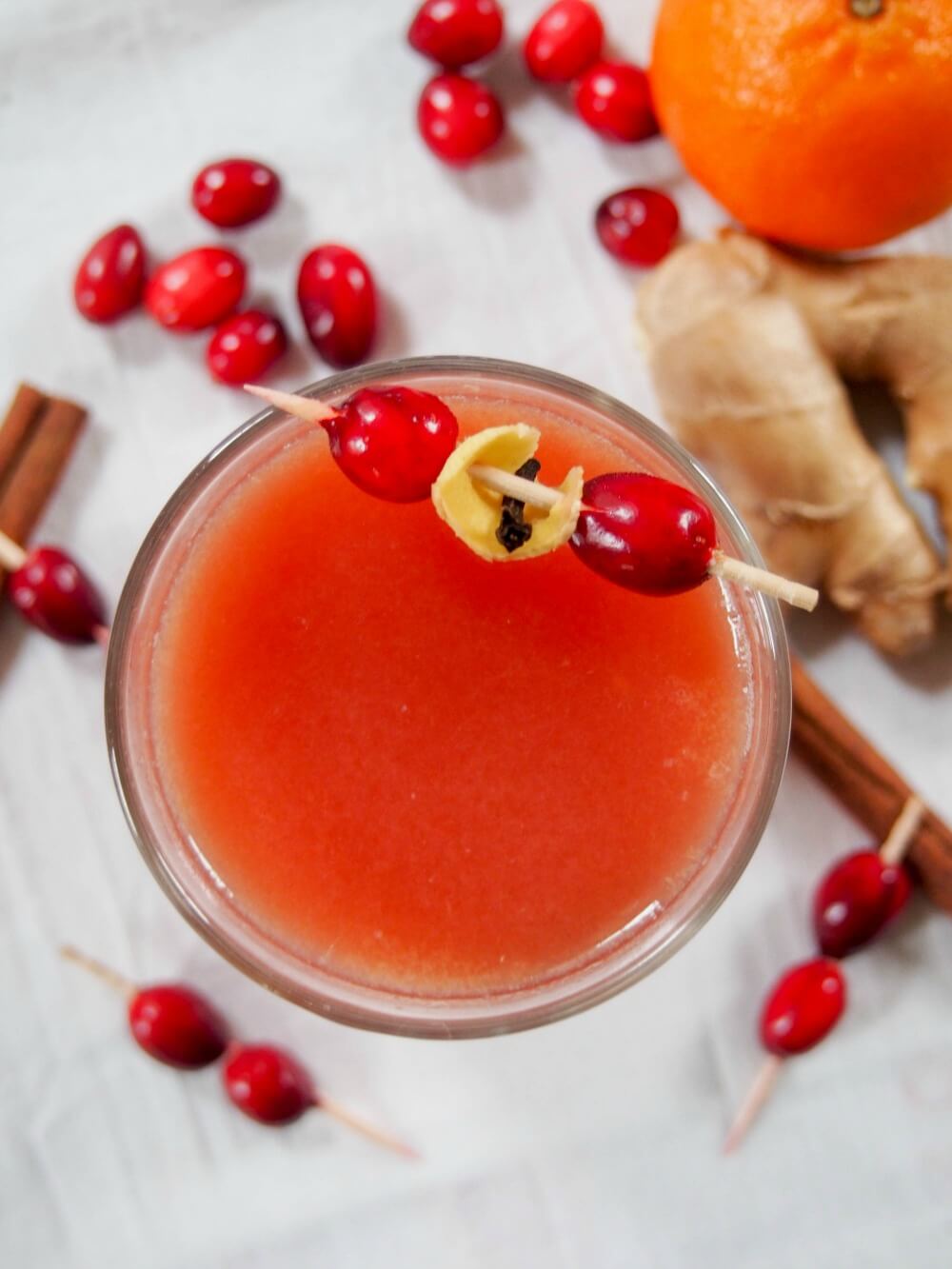 Warm spiced cranberry cocktail or mocktail viewed from overhead with ginger, cinnamon sticks and cranberries around glass
