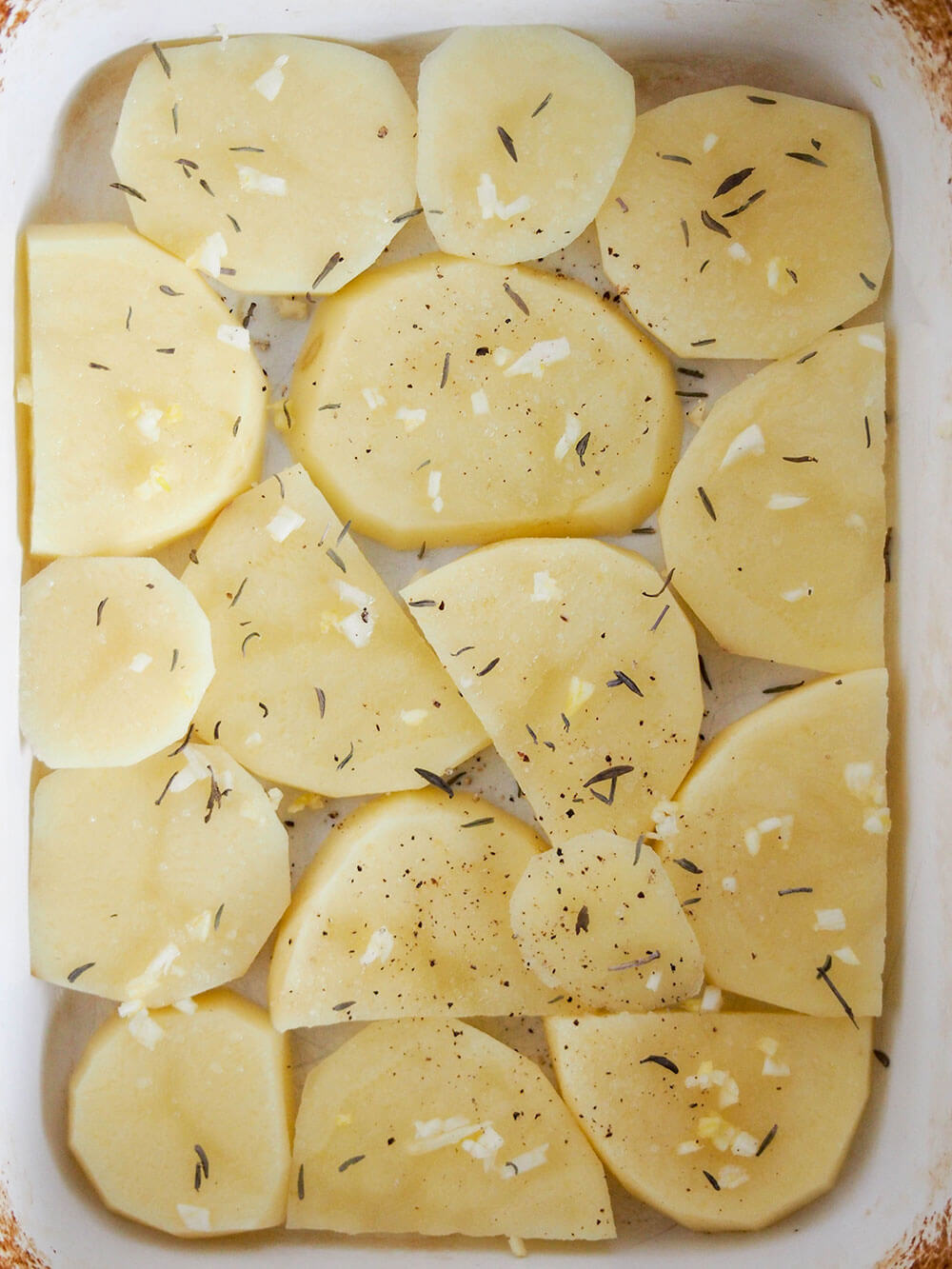 adding first layer of potatoes, thyme and garlic for Dauphinoise potatoes adding first layer of potatoes, thyme and garlic for Dauphinoise potatoes