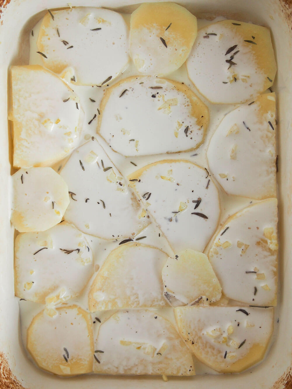 adding cream to layer of potatoes for Dauphinoise potatoes adding cream on top of potato layer